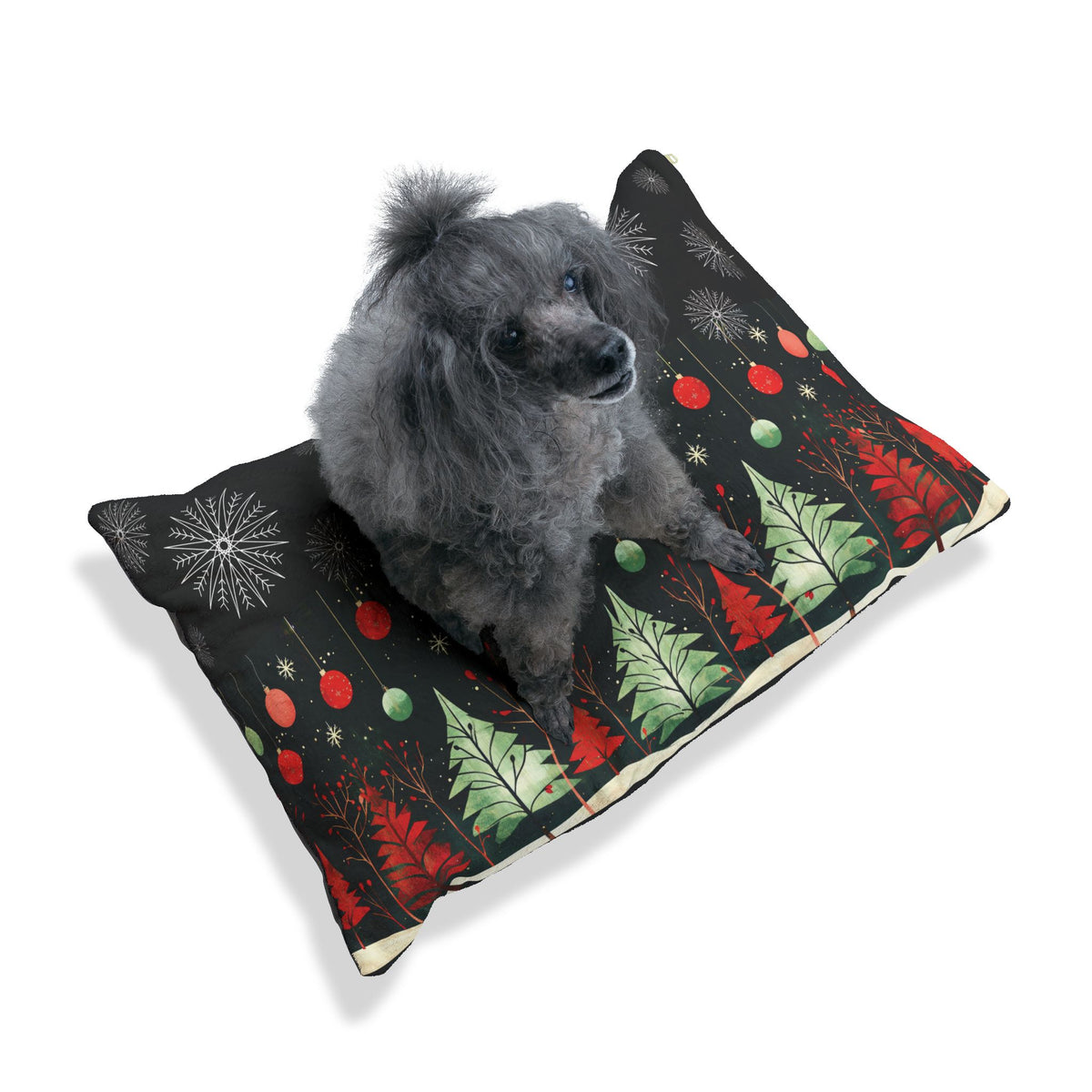 A small gray dog sits on a rectangular pet bed with a black background and a festive Christmas tree pattern in red, green, and white, photographed on a clean white background.