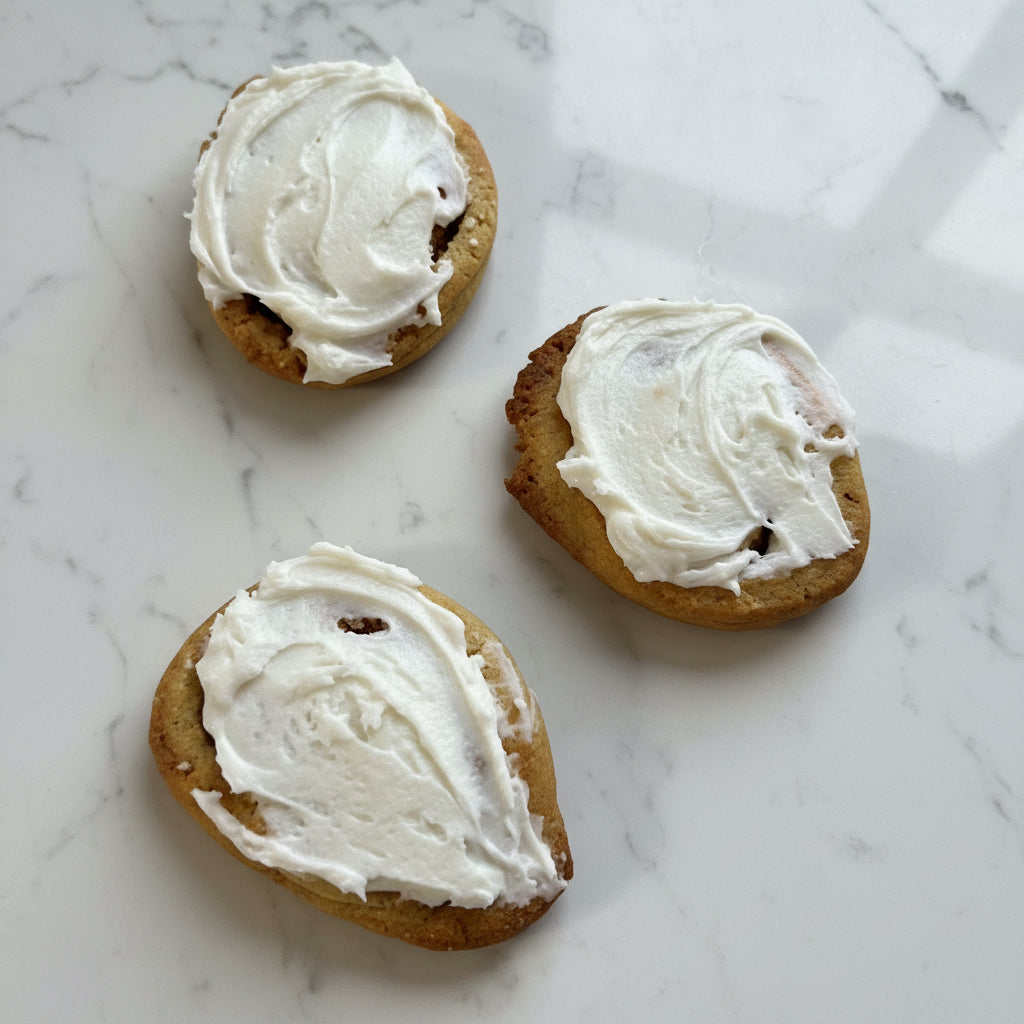 Three cookies with white frosting on a cooling rack.