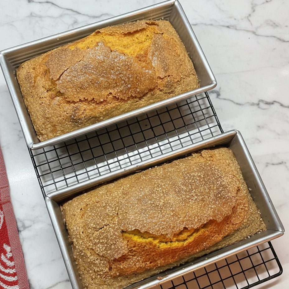 Two loaves of bread in metal pans on a cooling rack with a marble background