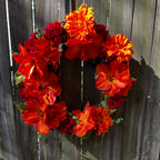 Floral wreath with orange and red flowers against a wooden fence.