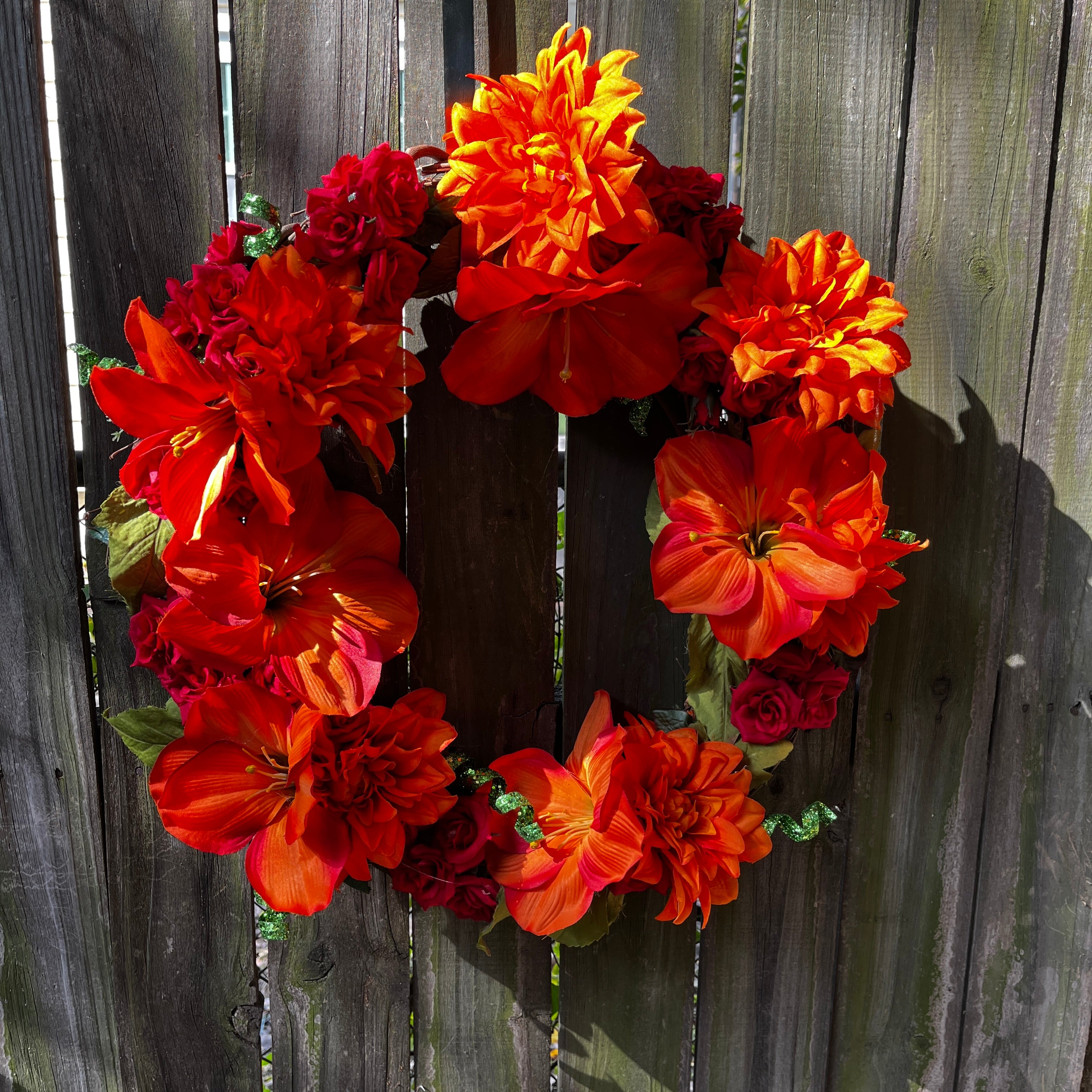 Floral wreath with orange and red flowers against a wooden fence.