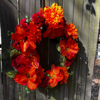 Floral wreath with orange and red flowers on a wooden fence