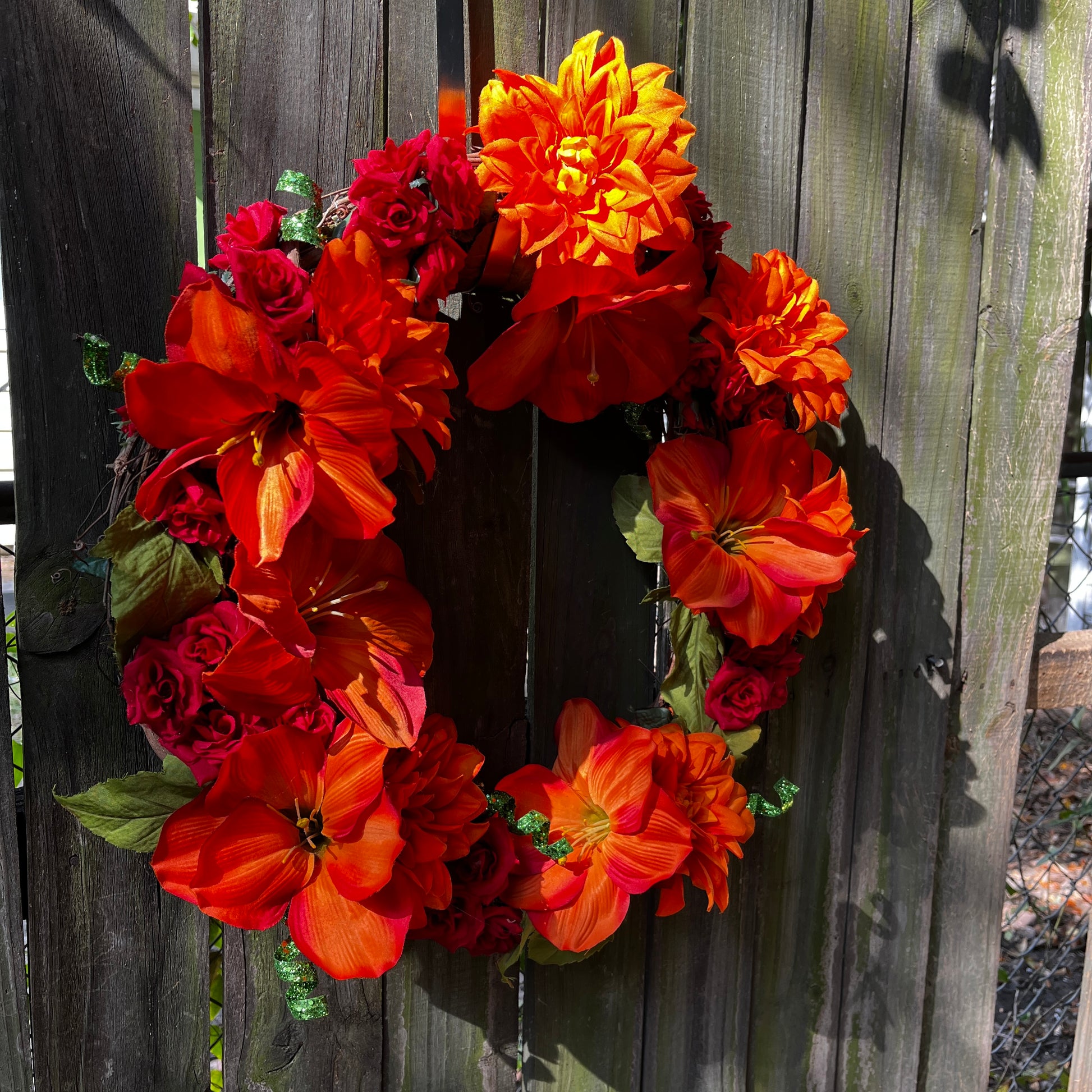 Floral wreath with orange and red flowers on a wooden fence