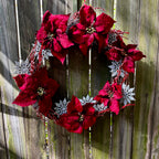 Decorative wreath with red flowers and silver snowflake accents on a wooden fence.
