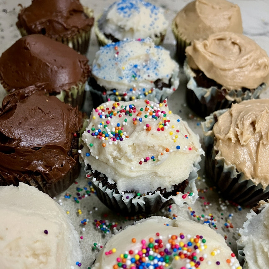 Assorted cupcakes with different frosting flavors and sprinkles on a metal tray.